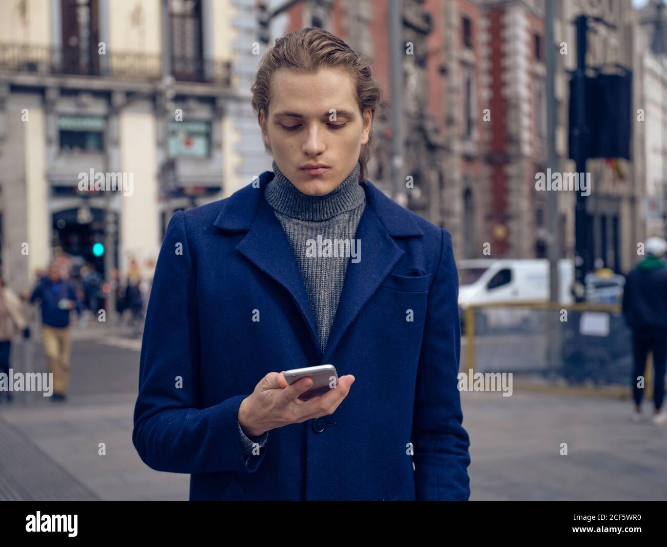 Jeune homme élégant qui navigue sur un smartphone dans la rue en ville rue Banque D'Images