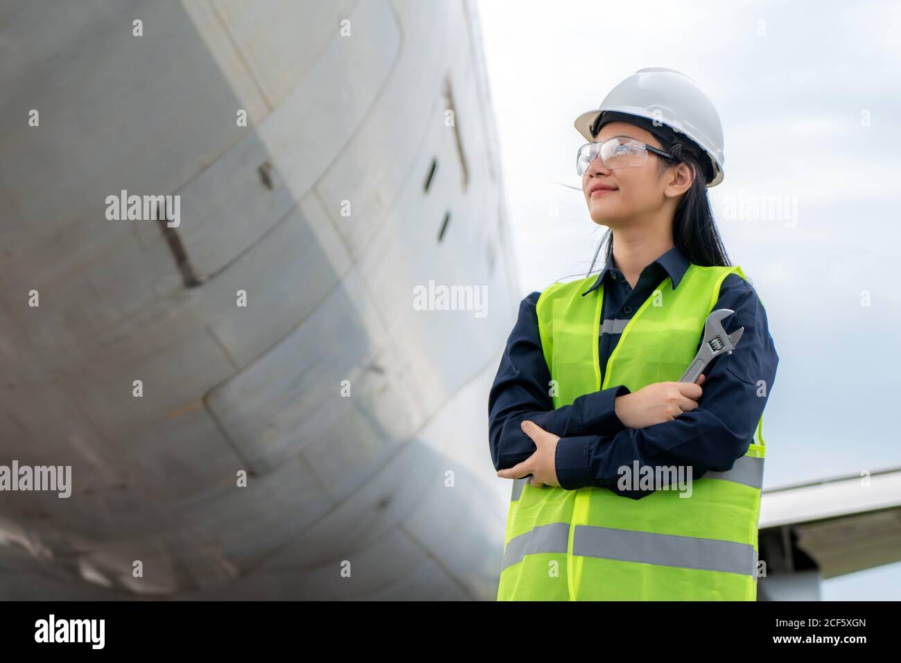 Femme asiatique ingénieur entretien bras d'avion croisé et tenant clé dans l'avion avant de réparations, de réparations, de modernisation et de rénovation dans airpor Banque D'Images