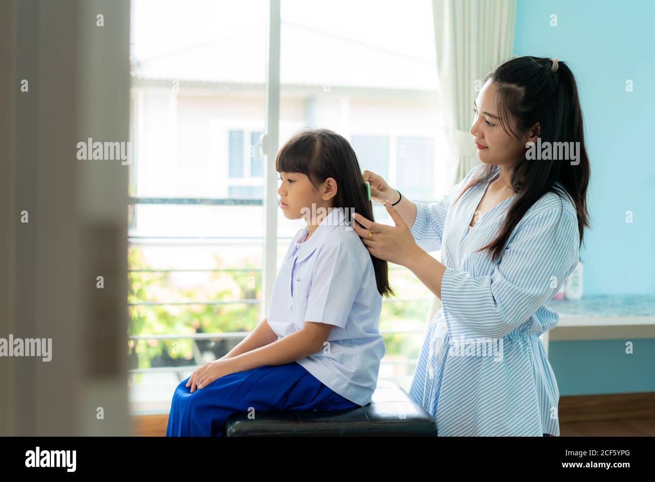 La mère asiatique peigne les cheveux de sa fille le matin avant d'aller à l'école dans le salon à la maison. La routine de l'école du matin pour la journée dans le li Banque D'Images