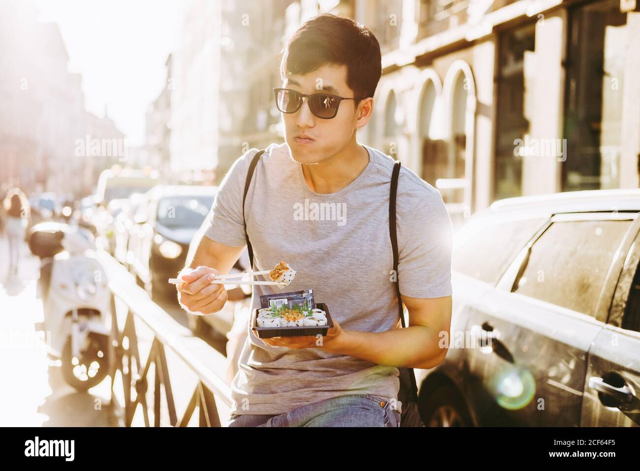 Homme asiatique élégant et ethnique en lunettes de soleil mangeant de la  nourriture à emporter avec baguettes debout près d'un camion sur une rue  ensoleillée Photo Stock - Alamy