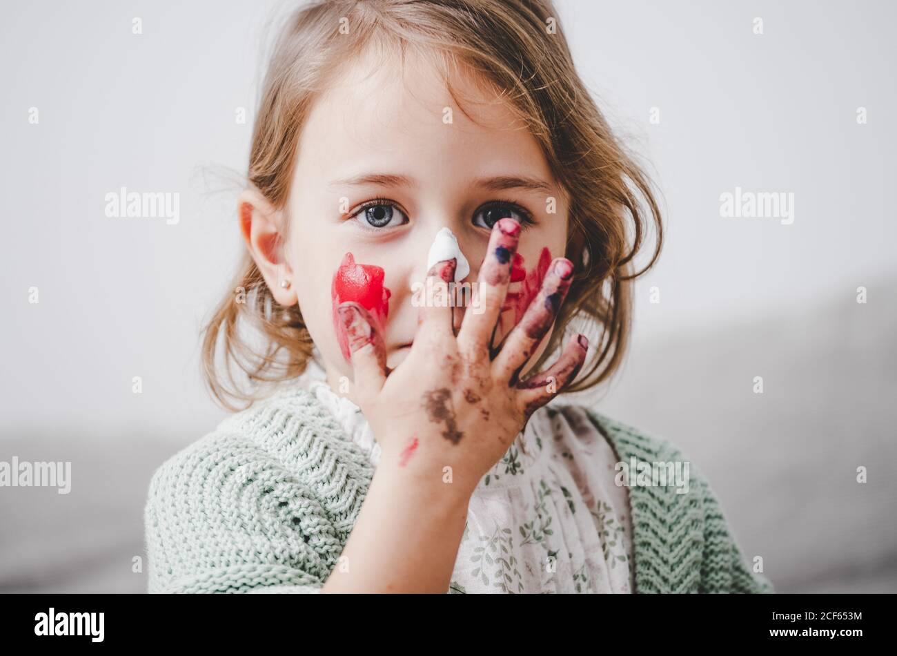 Drôle enfant avec les mains sales dans les peintures colorantes visage et regarder l'appareil photo sur un arrière-plan flou Banque D'Images