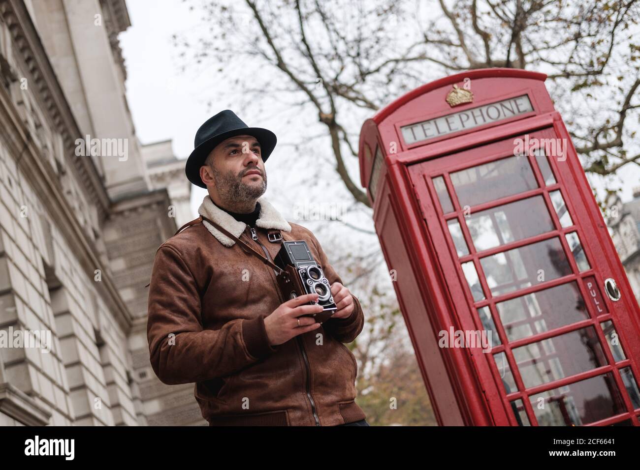 D'en dessous, un homme avec un appareil photo rétro regardant loin pendant situé sur la rue London, à proximité d'un téléphone rouge traditionnel Banque D'Images