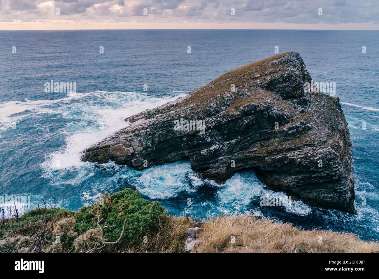 Vagues de mer mousseuse qui se roulent et se brisent près d'une roche rugueuse soirée nuageux dans la nature Banque D'Images