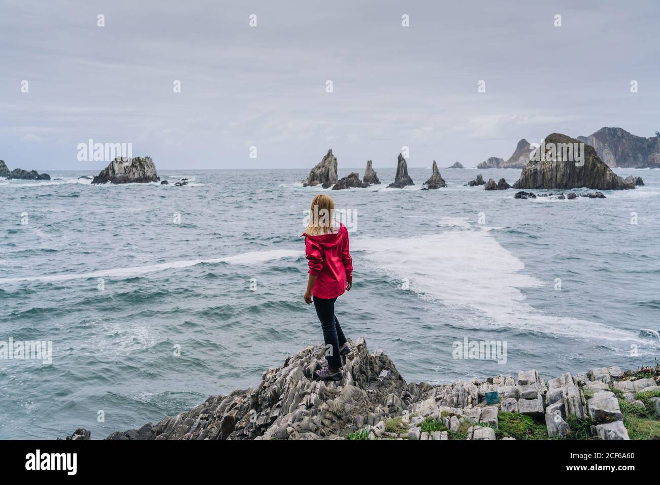 Femme sur un rivage pierreux regardant sur des pics de lavage d'eau mousseuse Banque D'Images