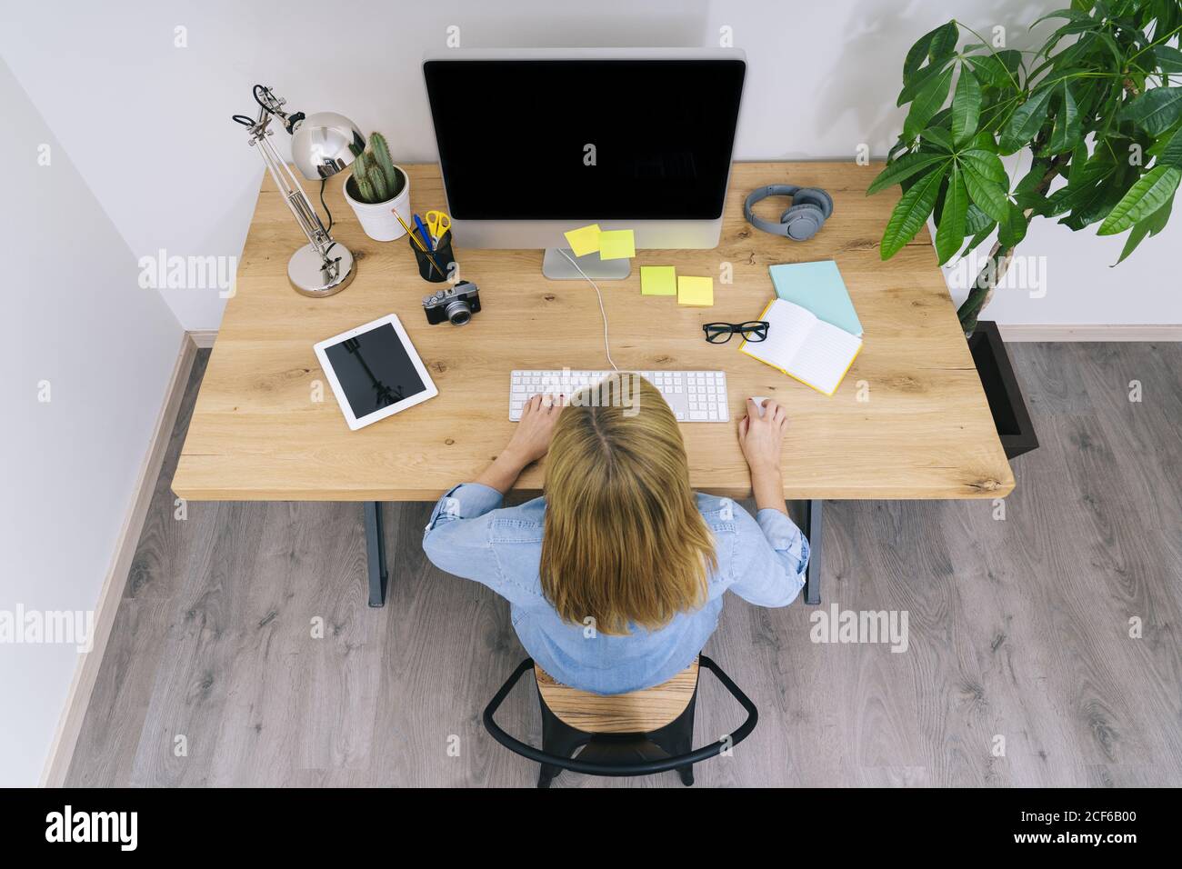 Vue de dessus de la femme blanche blonde anonyme dans des vêtements  décontractés assis sur un bureau en bois travaillant sur un ordinateur dans  un bureau à domicile moderne Photo Stock -