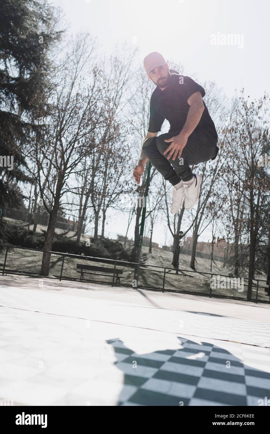 Vue latérale d'un jeune homme sautant et pratiquant la danse de pause sur un plancher à carreaux dans le parc par temps ensoleillé Banque D'Images