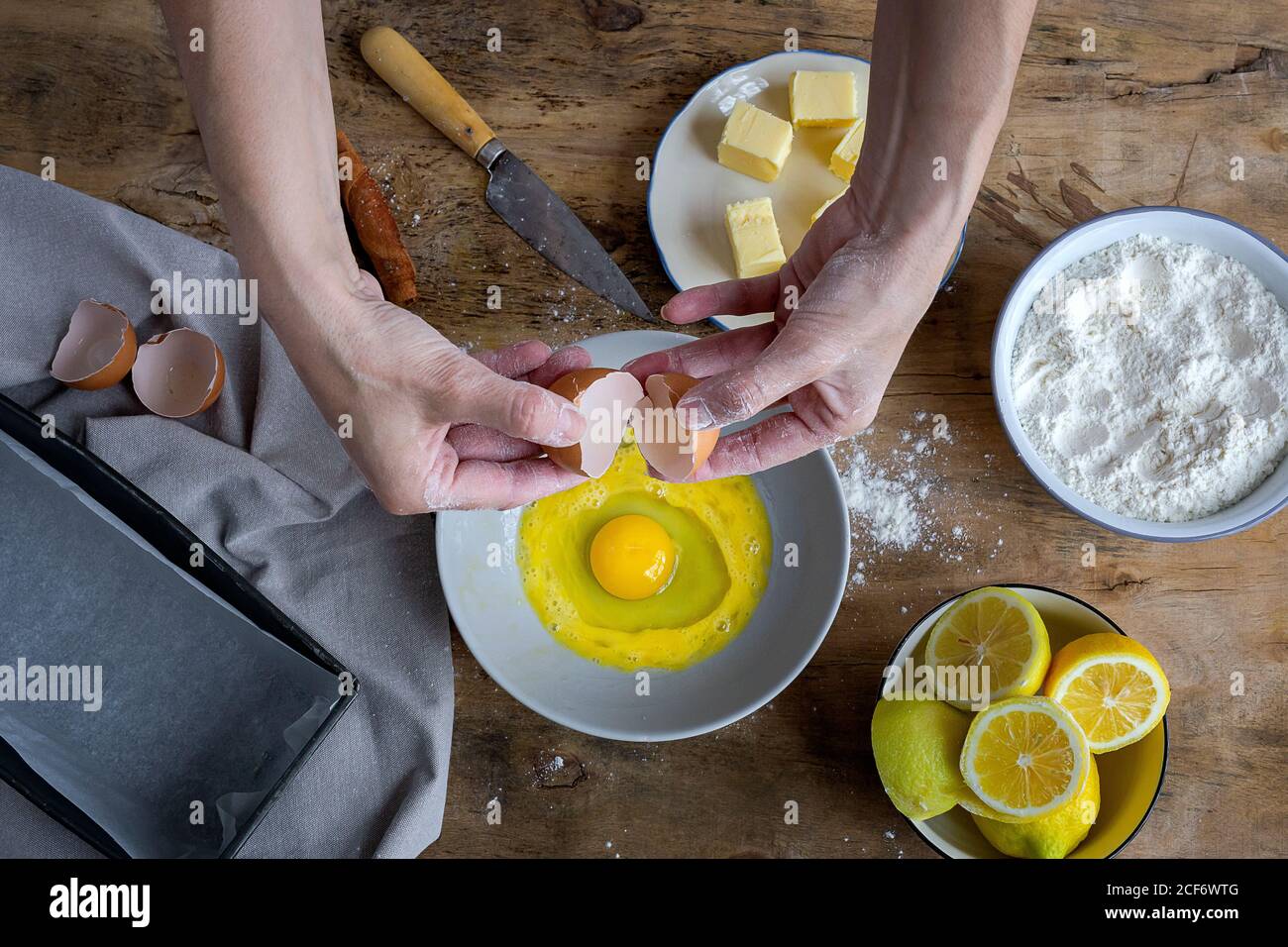 De dessus vue de dessus de dessus de dessus la femelle brisant l'oeuf frais de poulet dans un bol tout en cuisant la pâtisserie dans une table en bois avec ingrédients frais Banque D'Images