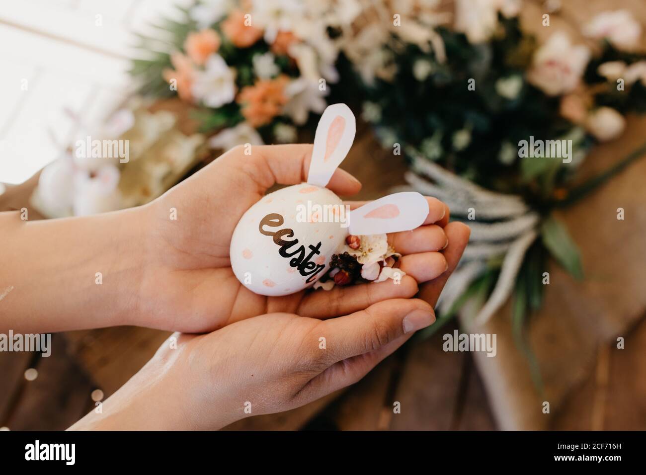 jeune femme tenant un oeuf de pâques avec des oreilles de lapin peintes par les enfants avec des fleurs Banque D'Images