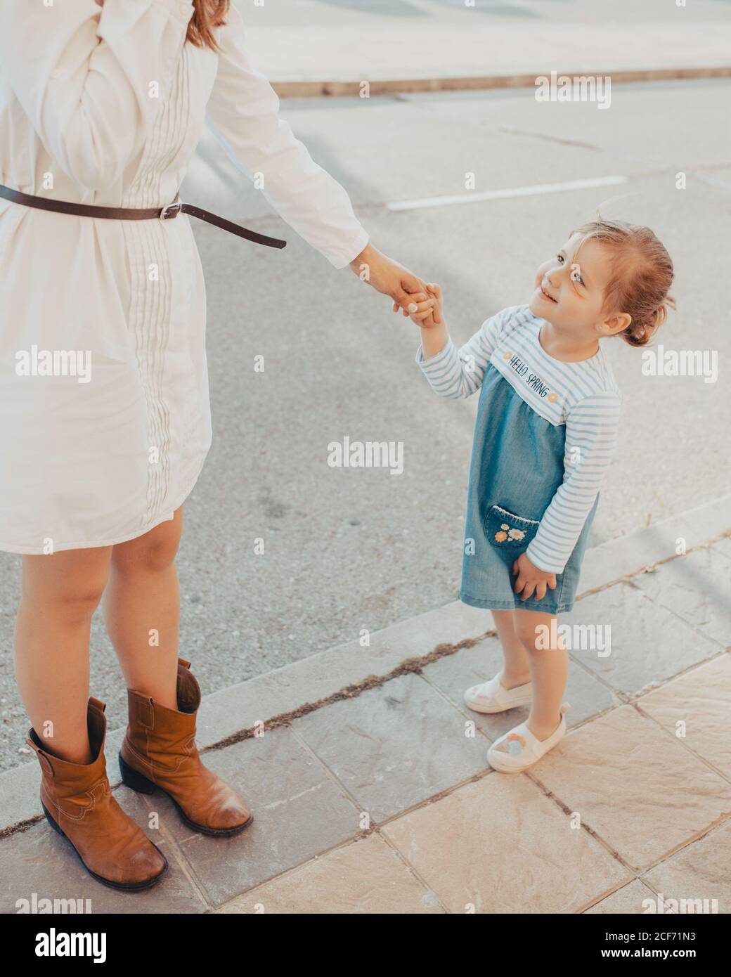 Une jeune femme anonyme et une petite fille tenant les mains et debout sur  le trottoir ensemble contre un ciel bleu sans nuages sur la rue de la ville  Photo Stock -