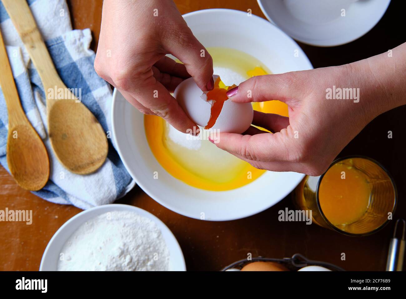 Femme méconnaissable cassant l'œuf de poulet cru sur un bol avec du sucre près de la farine de blé pendant la préparation de la pâtisserie à la maison Banque D'Images