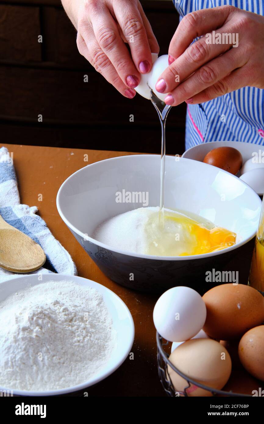 Femme méconnaissable cassant l'œuf de poulet cru sur un bol avec du sucre près de la farine de blé pendant la préparation de la pâtisserie à la maison Banque D'Images