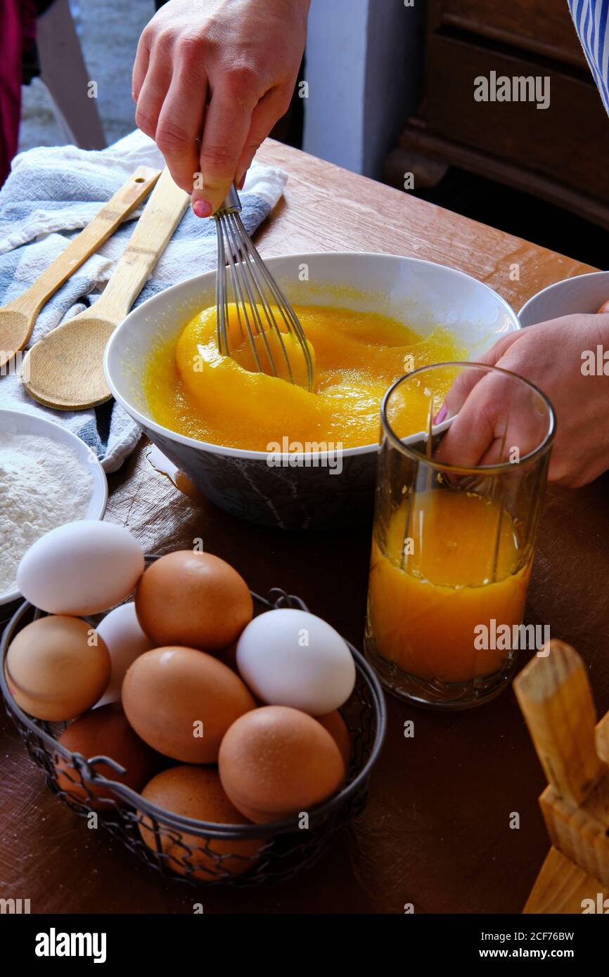 De la récolte ci-dessus femelle à l'aide d'un fouet pour mélanger le sucre avec œufs crus près d'une tasse de jus d'agrumes pendant la cuisson de la pâtisserie sur une table de cuisine Banque D'Images