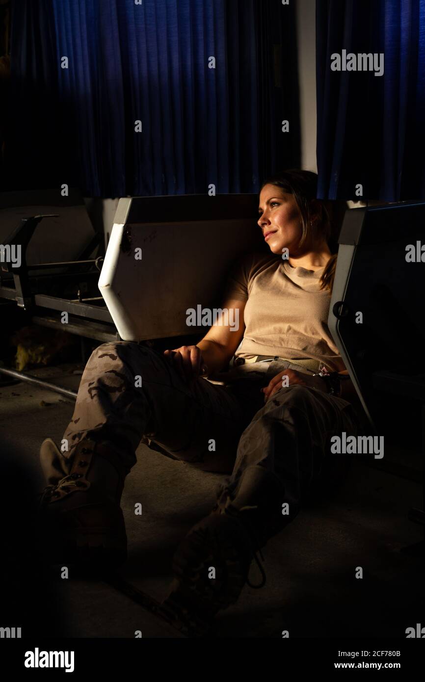 Femme militaire sérieuse en uniforme regardant loin tout en étant assis sur le plancher de transport de l'armée Banque D'Images