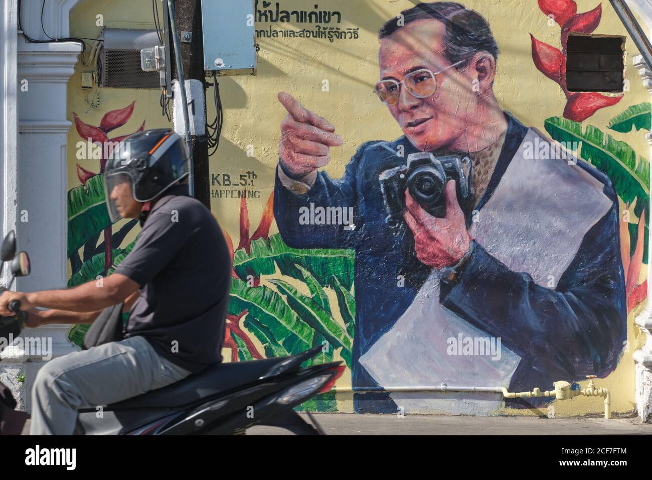 Un chauffeur de moto passe devant un portrait du roi thaïlandais Bhumipol Adulyadej, peint sur les murs de la vieille ville de Phuket, en Thaïlande Banque D'Images