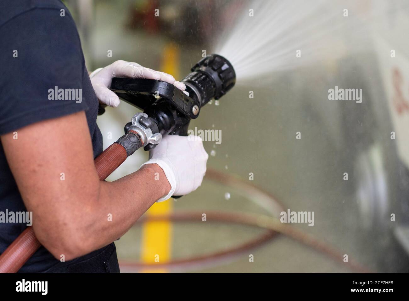 Vue latérale d'un pompier méconnaissable dans une voiture de lavage avec gants en latex avec tuyau d'incendie à la station Banque D'Images