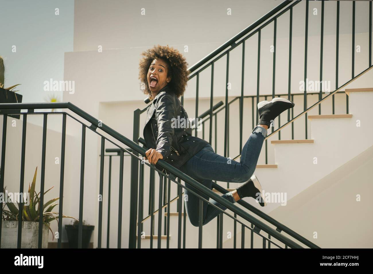 Vue latérale d'une femme afro-américaine excitée regardant la caméra et crier tout en se penchant sur les rampes et en sautant sur le bâtiment escaliers Banque D'Images