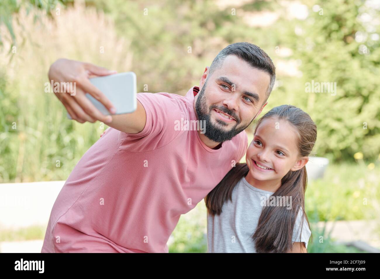 Jeune père adulte moderne portant un T-shirt rose pâle prenant un selfie tourné avec sa fille, horizontal moyen Banque D'Images