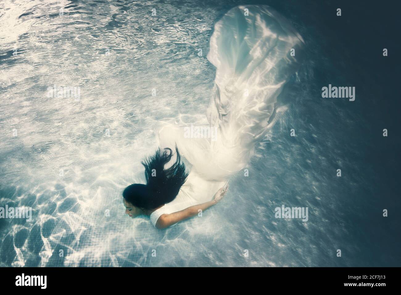 Magnifique brunette aux cheveux longs en robe de mariage blanche longue  avec voile flottant sous l'eau avec bras étirés Photo Stock - Alamy