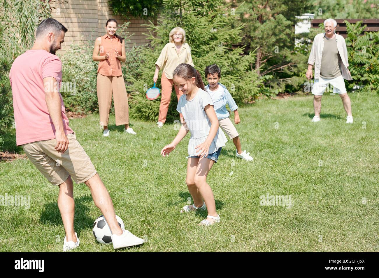 Granpa, papa et deux enfants jouant au football sur pelouse dans le parc, grand-mère et mère les regardant Banque D'Images