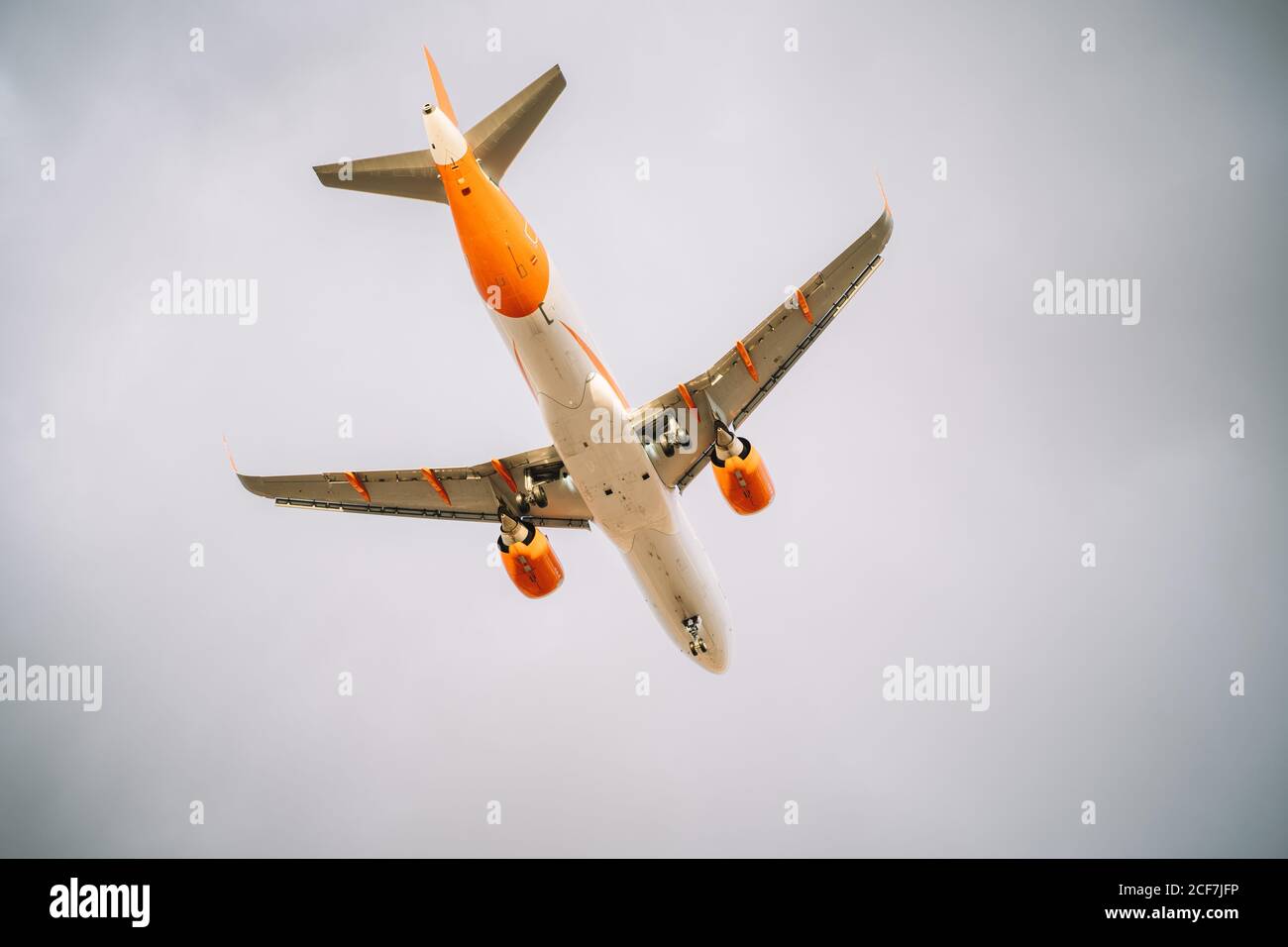 De dessous d'avion blanc et orange volant avec ciel nuageux ciel gris sur fond Banque D'Images