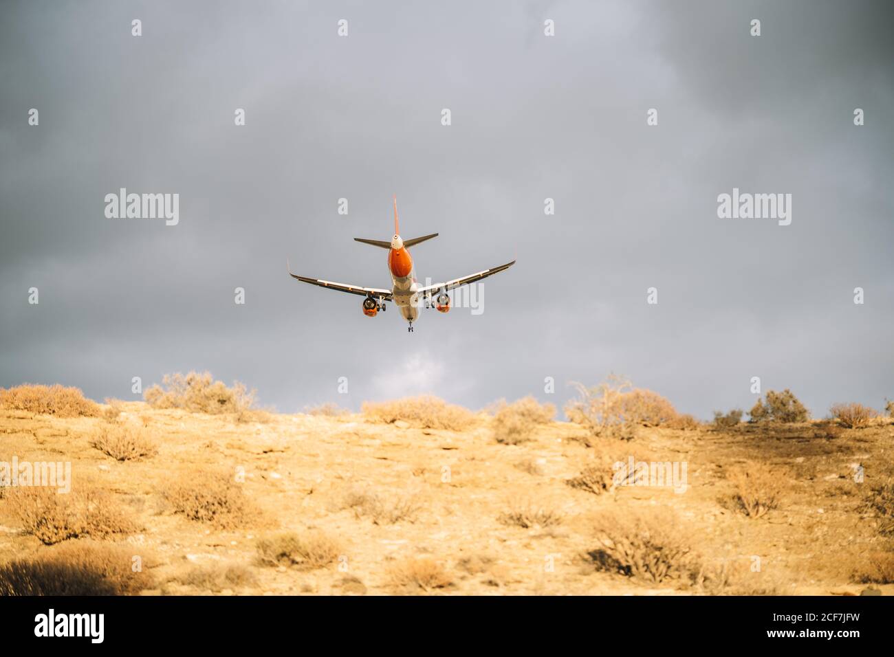 De dessous d'avion blanc et orange volant avec ciel nuageux ciel gris sur fond Banque D'Images