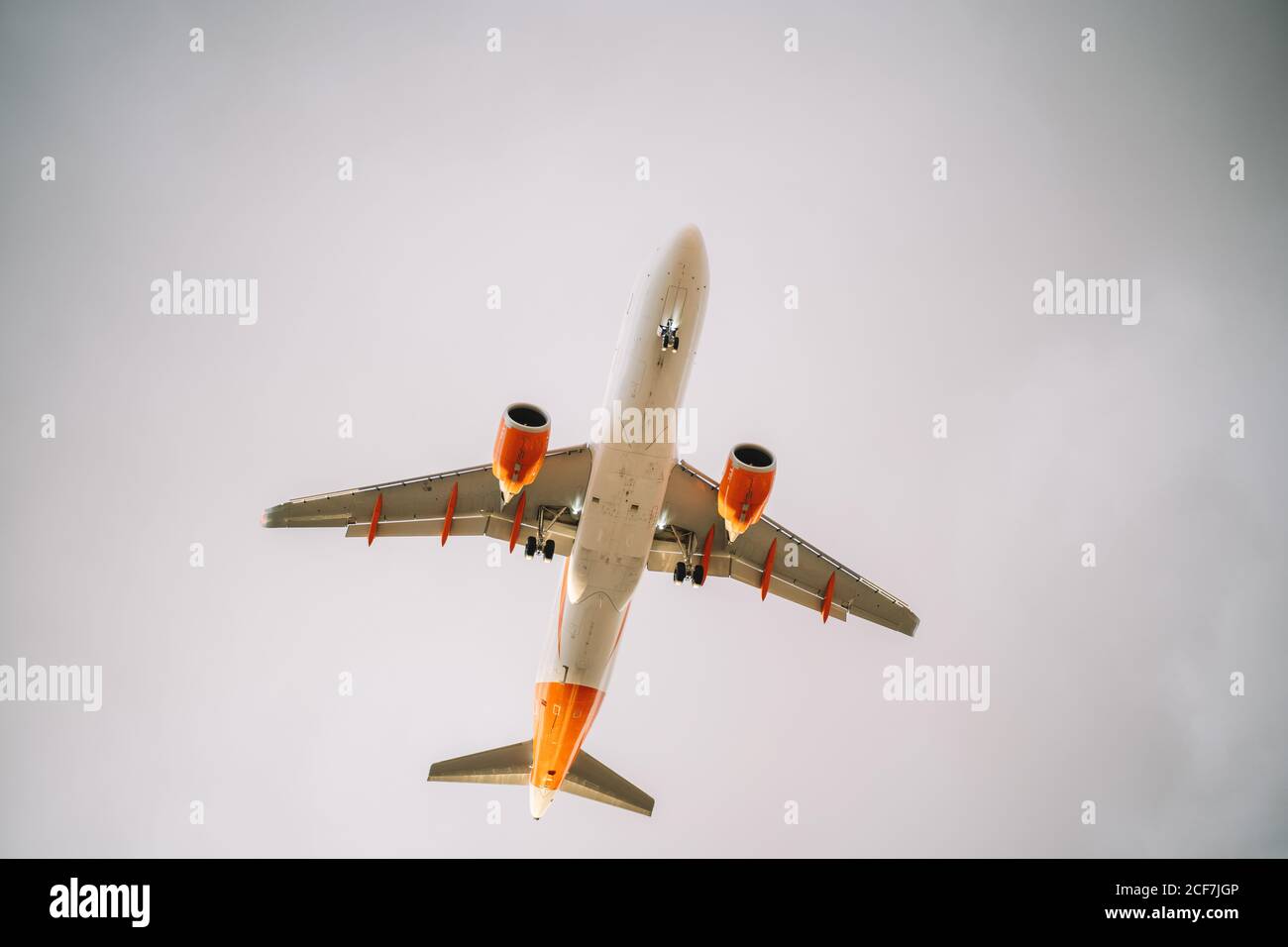 De dessous d'avion blanc et orange volant avec ciel nuageux ciel gris sur fond Banque D'Images