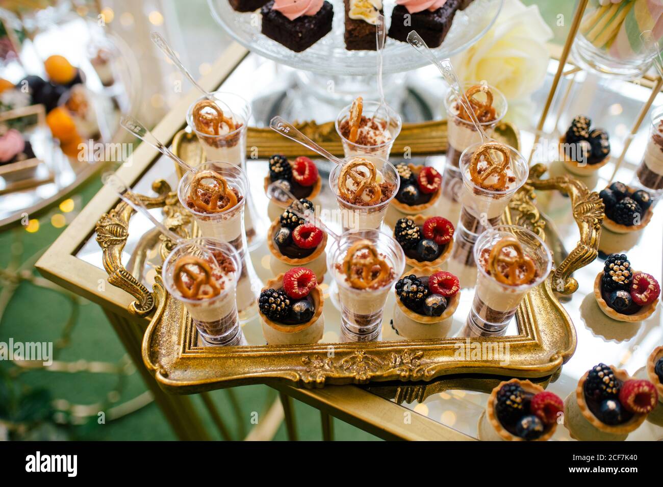 De dessus décoré doux et savoureux cheesecake shooters sur plateau doré et gâteau à fleurs roses sur support en verre dans le restaurant Banque D'Images