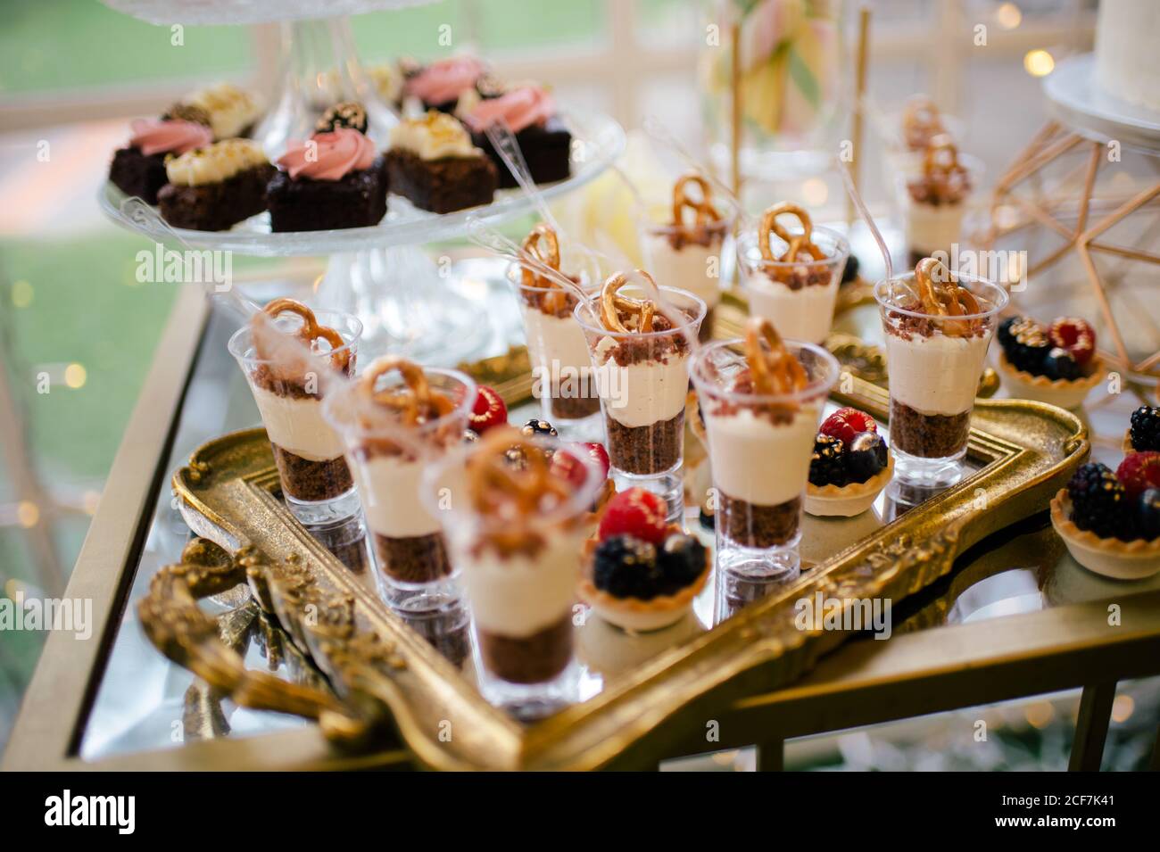 De dessus décoré doux et savoureux cheesecake shooters sur plateau doré et gâteau à fleurs roses sur support en verre dans le restaurant Banque D'Images
