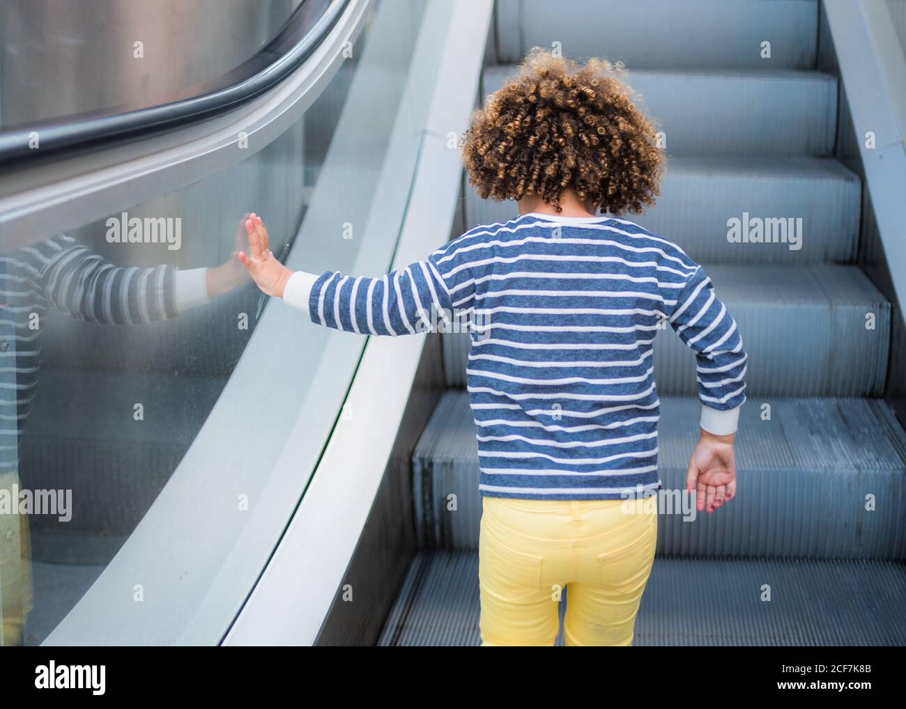 Vue arrière de la petite fille à poil dur ethnique méconnue tenue tendance sur l'escalier de l'escalier mécanique en ville Banque D'Images