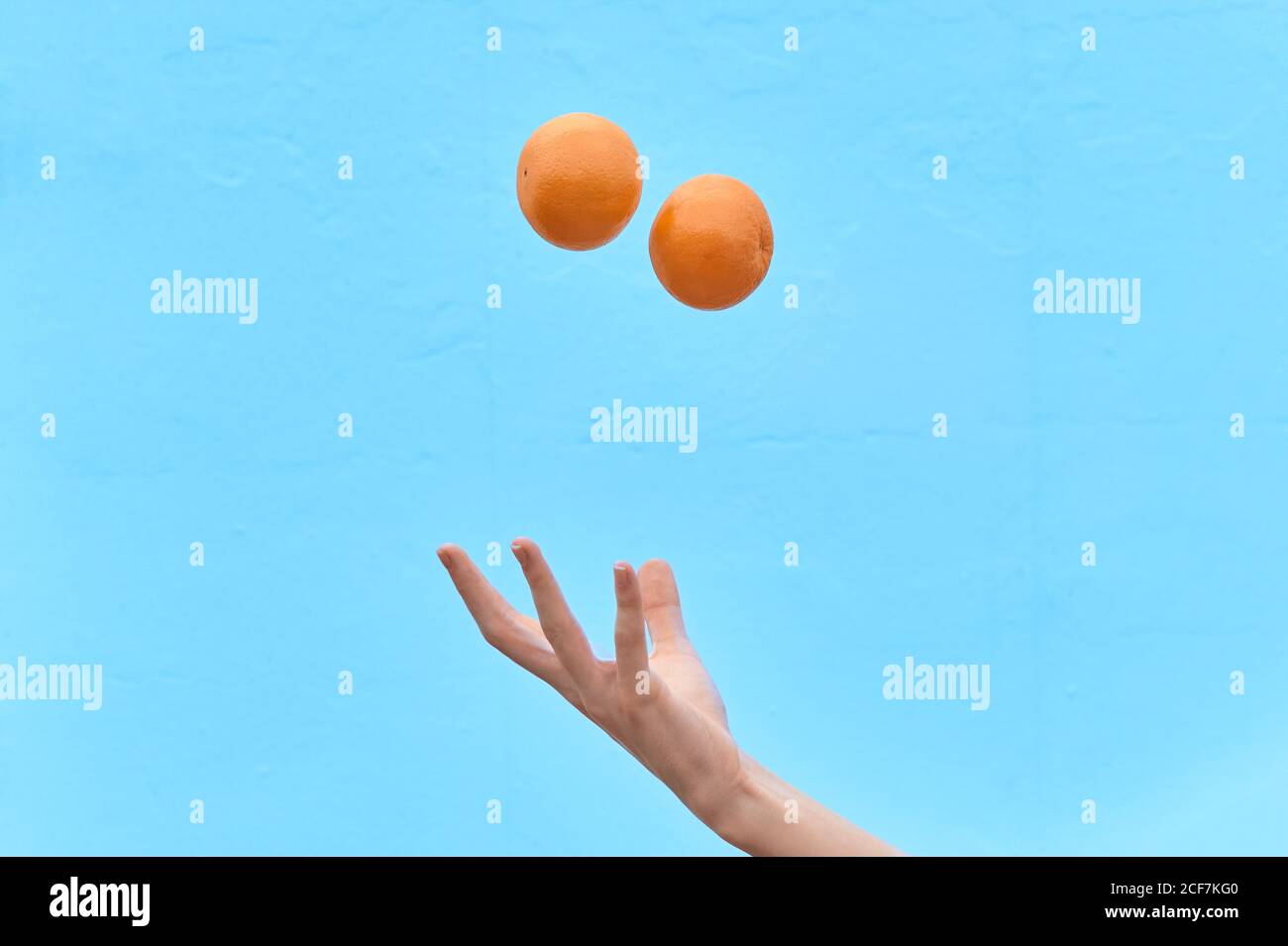 La femme de culture lance de l'orange frais dans l'air montrant le concept de régime sain sur fond bleu Banque D'Images
