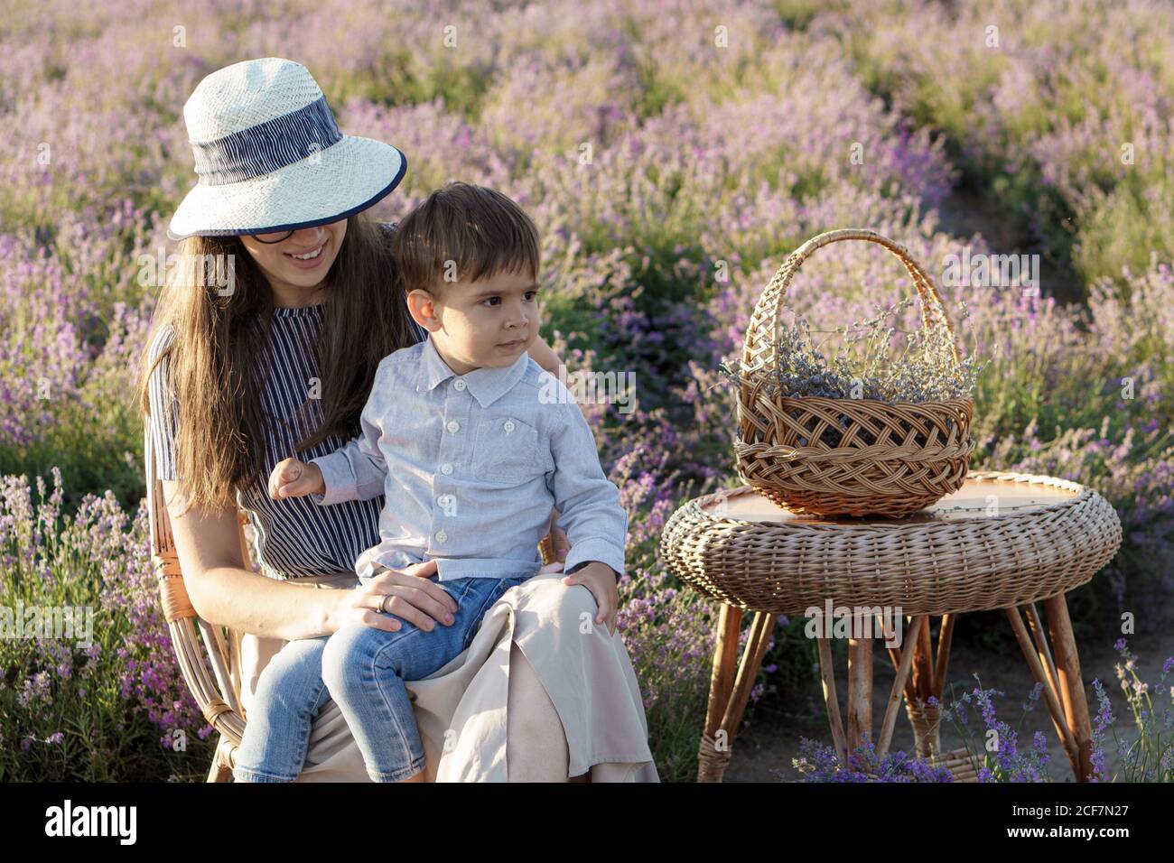 Grande famille, paternité, enfance, maternité, concept de style provençal - jeune maman est assise sur une chaise en osier avec petit garçon enfant fils avec panier et table Banque D'Images