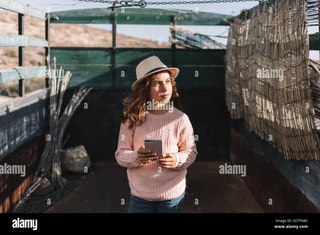 Fille concentrée regardant loin dans la paille chapeau rose pull tricoté et  jeans debout dans le corps de camion et de navigation de téléphone mobile  par temps venteux Photo Stock - Alamy