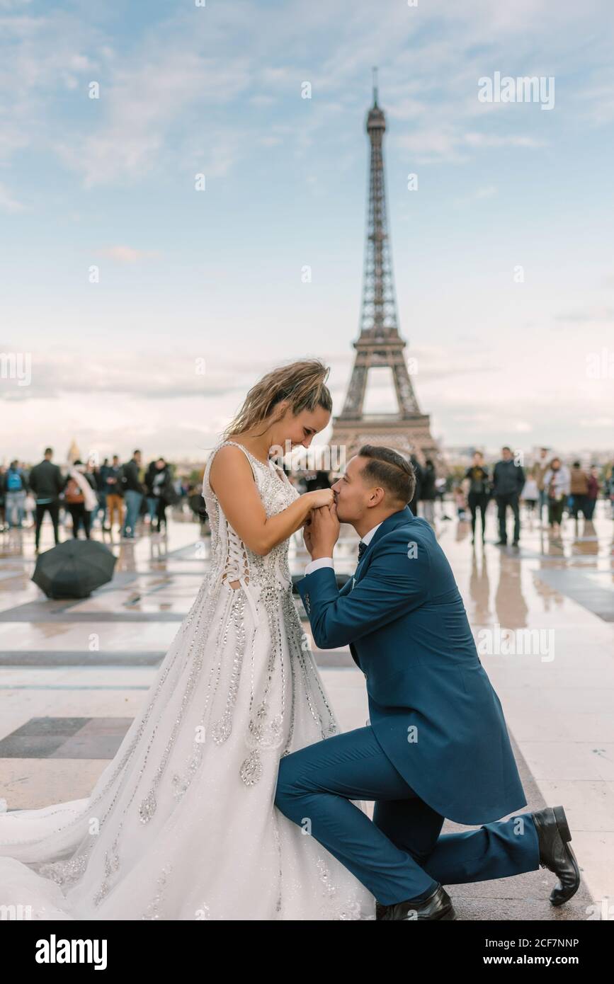 Tenue élégante bleue sur le genou et embrasser les mains de la mariée  satisfaite en robe de mariage blanche avec La Tour Eiffel en arrière-plan  Photo Stock - Alamy