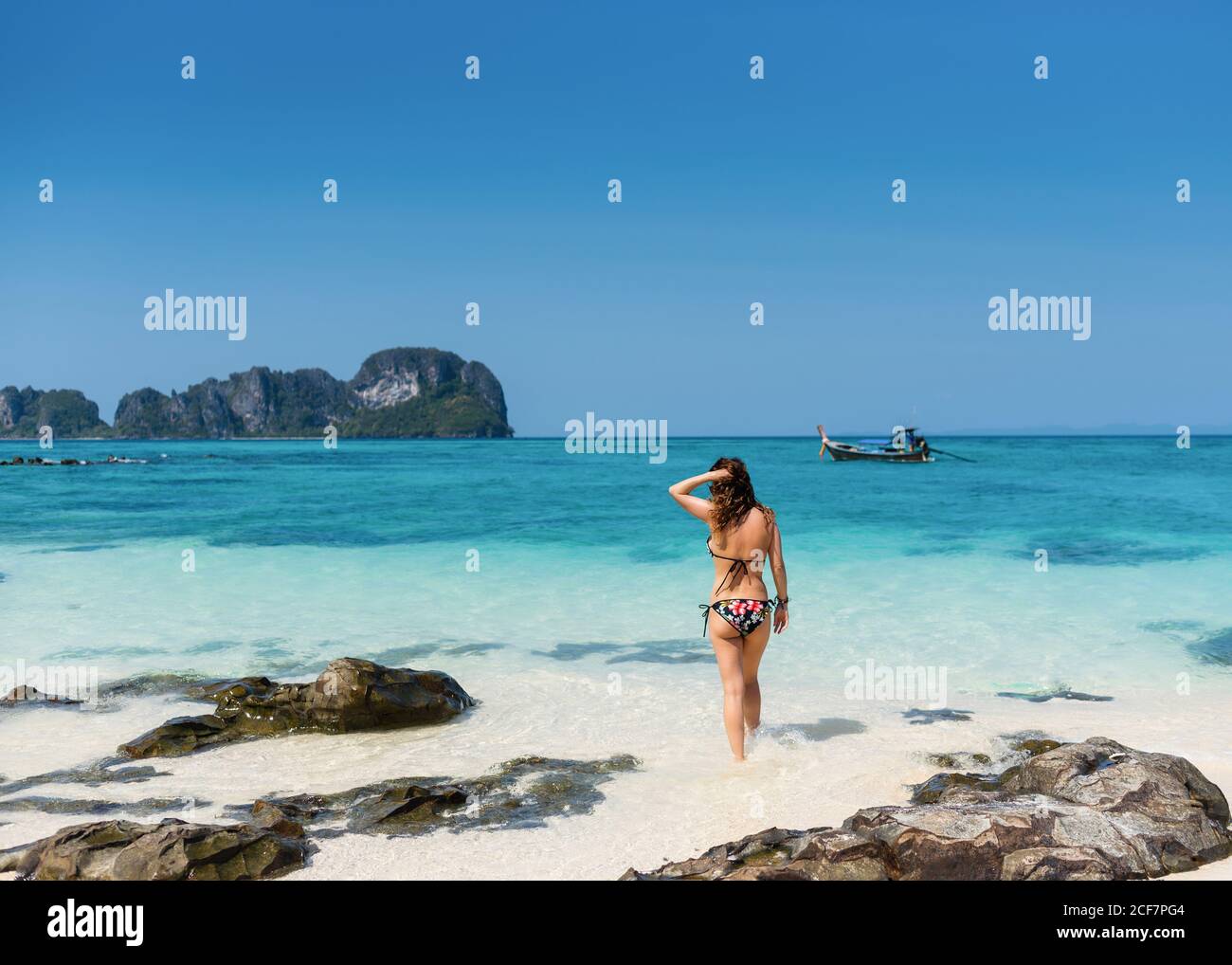 Vue arrière de la femme touristique mince en maillot de bain debout Côte sablonneuse de l'océan turquoise sous le ciel bleu en Thaïlande Banque D'Images