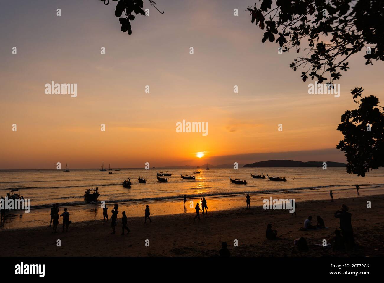Silhouettes de personnes méconnaissables marchant sur une plage de sable et des bateaux Sur la mer ondulée pendant le beau coucher de soleil en Thaïlande Banque D'Images