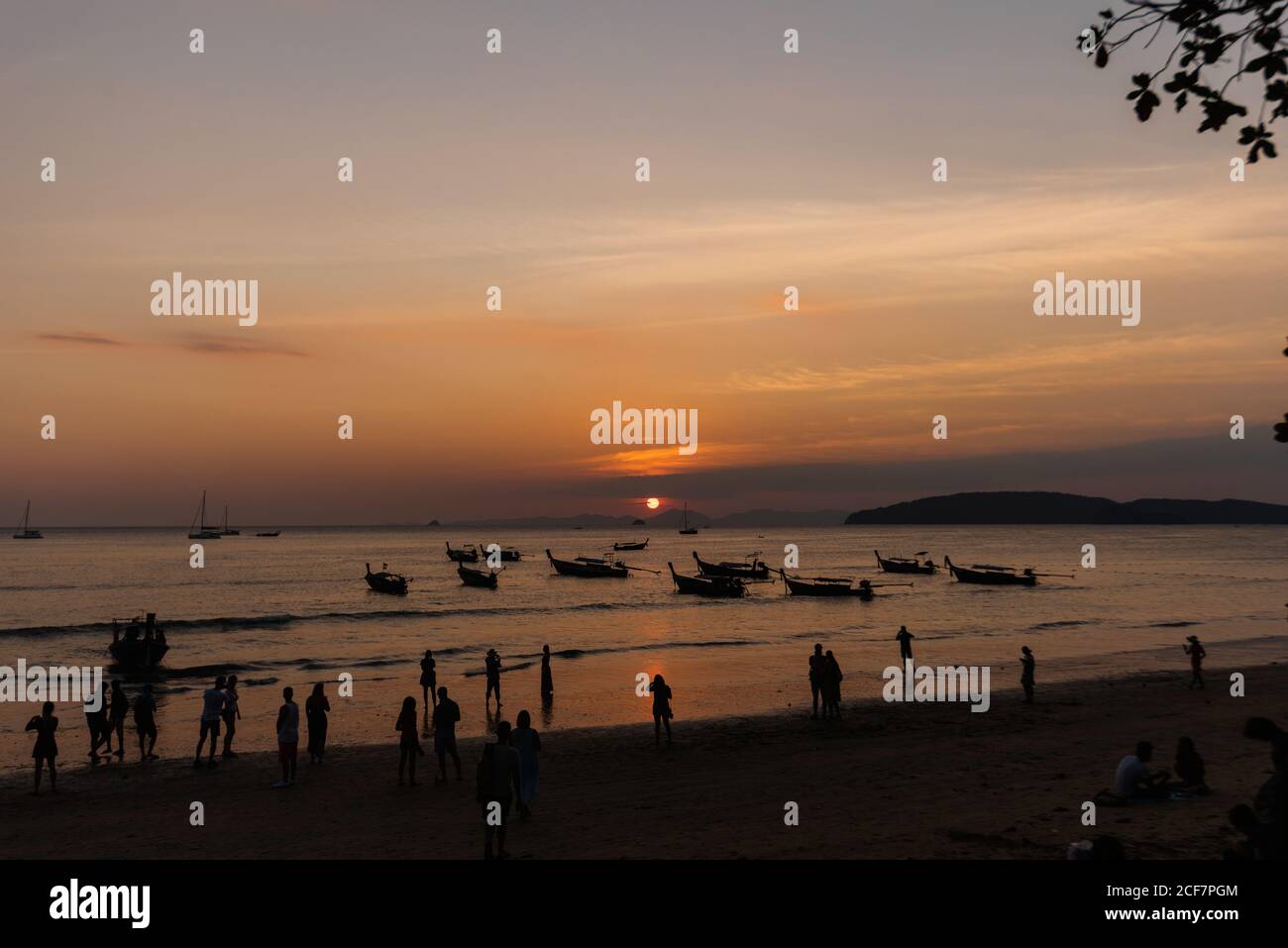 Silhouettes de personnes méconnaissables marchant sur une plage de sable et des bateaux Sur la mer ondulée pendant le beau coucher de soleil en Thaïlande Banque D'Images