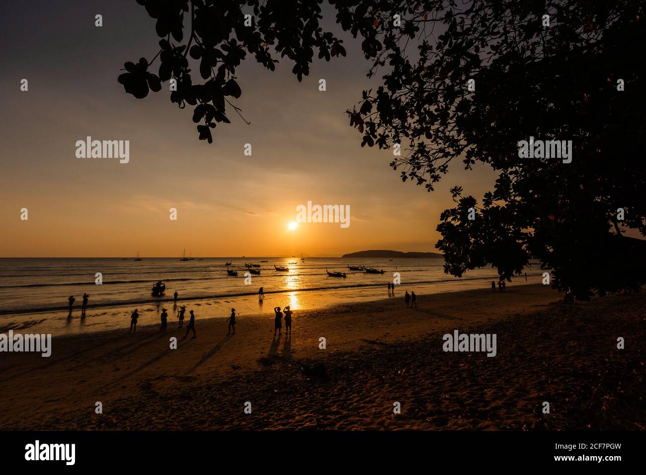 Silhouettes de personnes méconnaissables marchant sur une plage de sable et des bateaux Sur la mer ondulée pendant le beau coucher de soleil en Thaïlande Banque D'Images