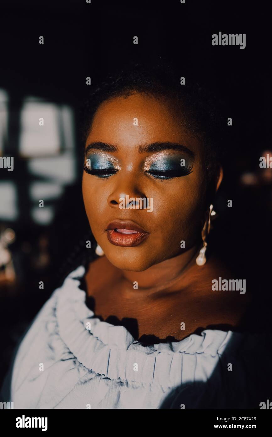 Portrait de rétro-éclairé beau curvy noir jeune femme avec lumineux maquillage dans la robe hors-épaule en regardant vers le bas Banque D'Images