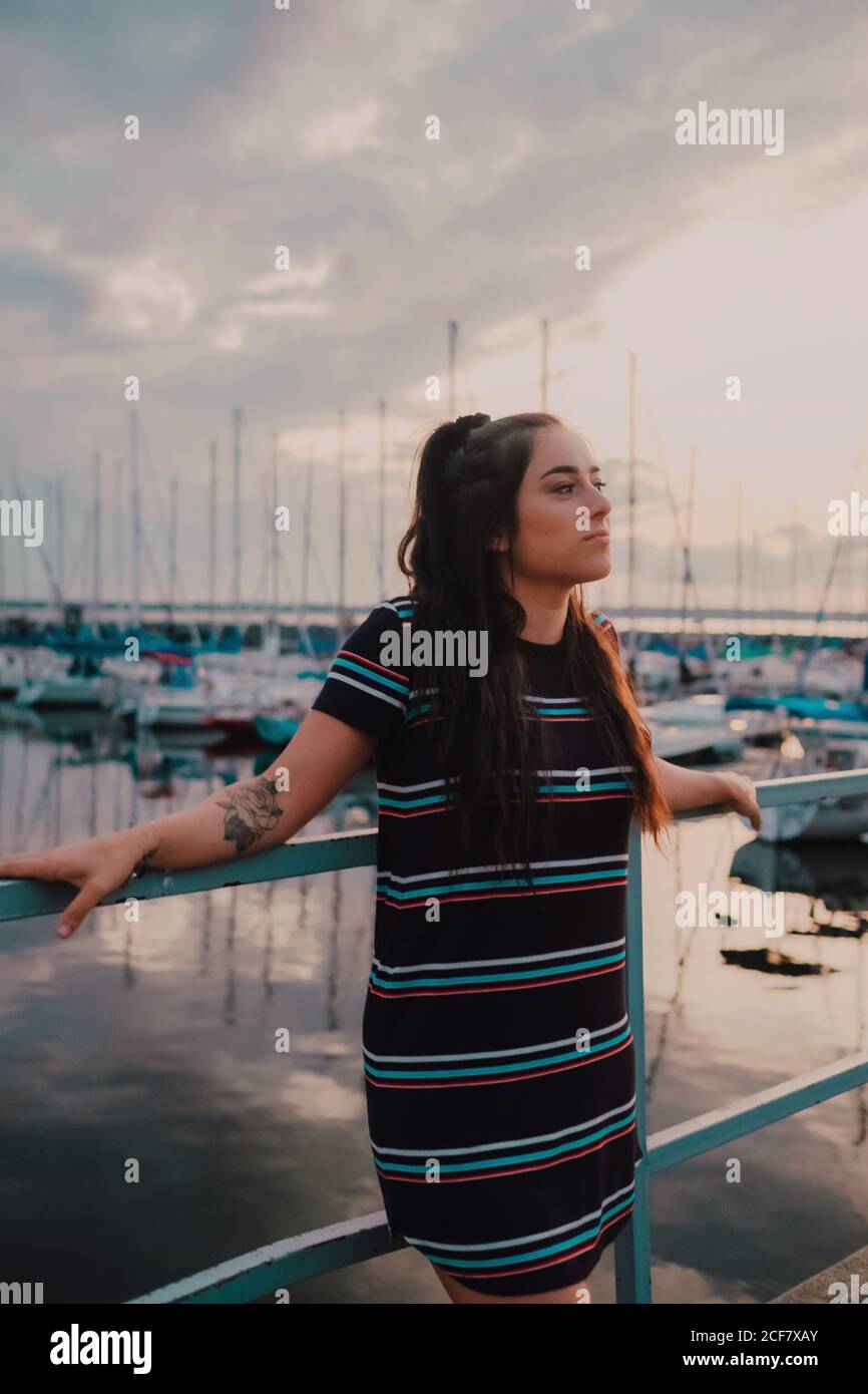 Bonne jeune femme tatouée en robe debout sur le quai rempli de yachts et de bateaux Banque D'Images