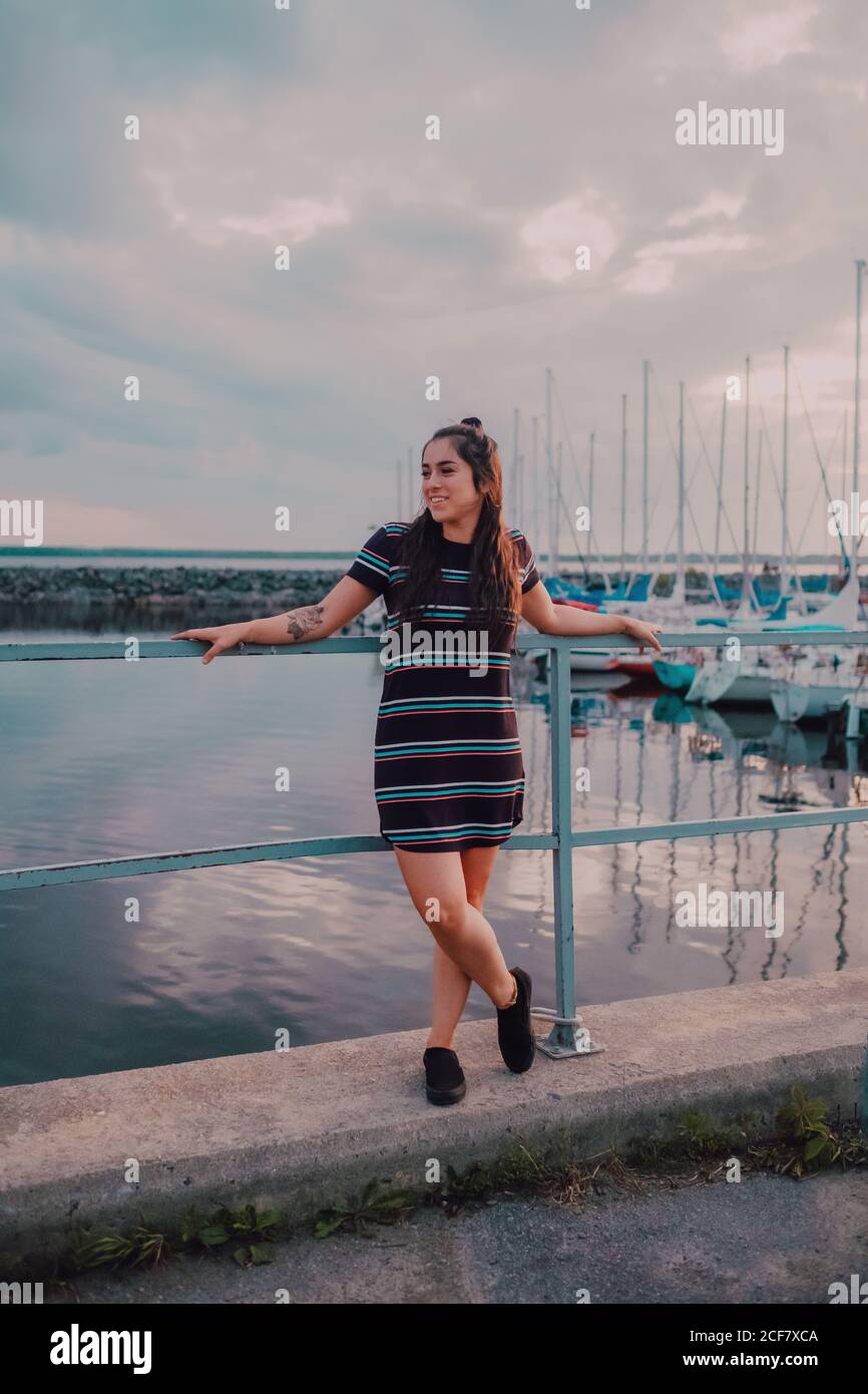 Bonne jeune femme tatouée en robe debout sur le quai rempli de yachts et de bateaux Banque D'Images