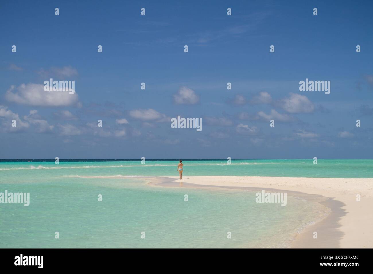 Vue arrière de la dame éloignée se tenant sur la plage de sable à proximité Magnifique mer turquoise par jour nuageux aux Maldives Banque D'Images