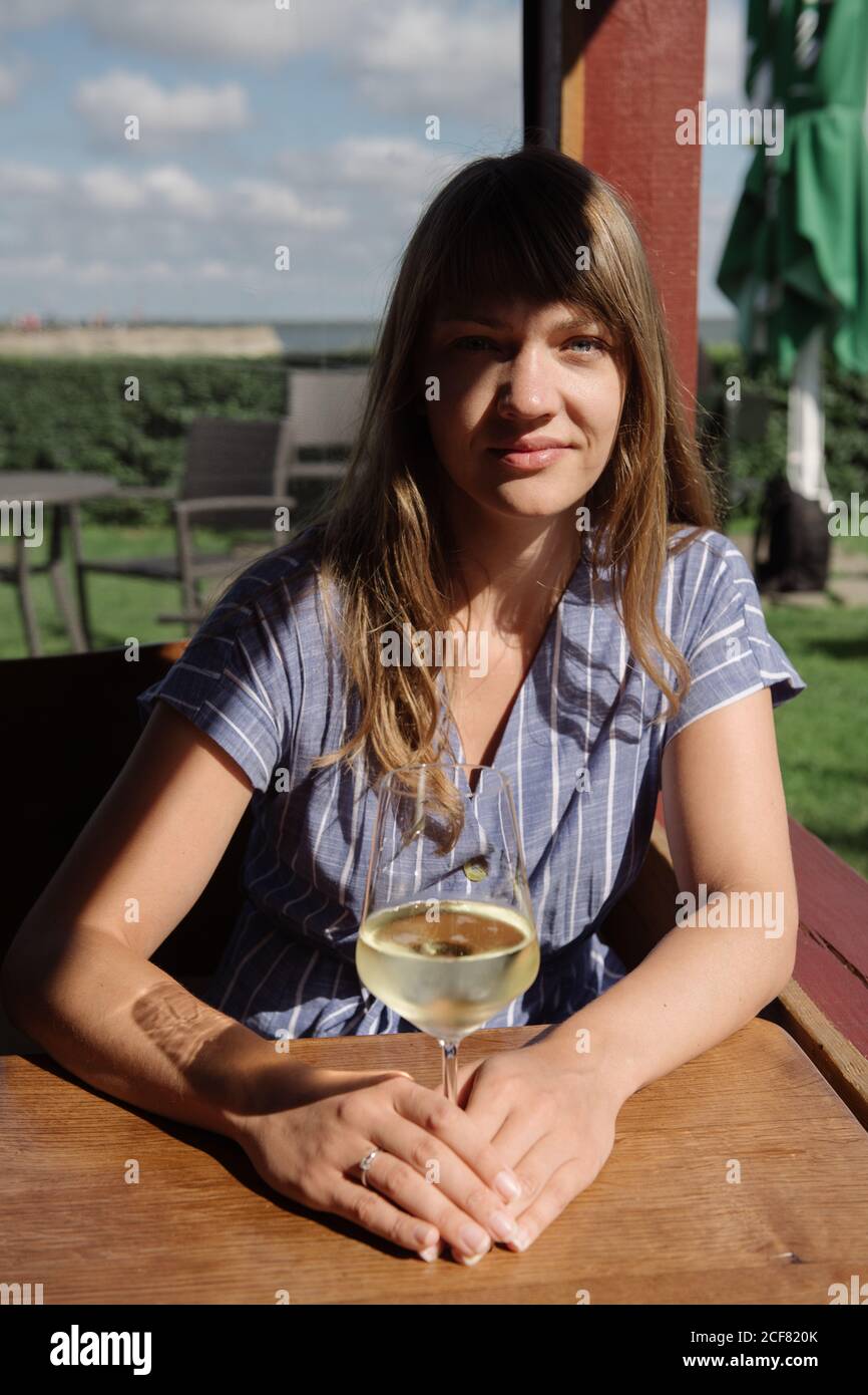Femme adulte en robe tenant le verre sur le vin blanc tout en étant assise à table dans l'arbre le jour ensoleillé Banque D'Images