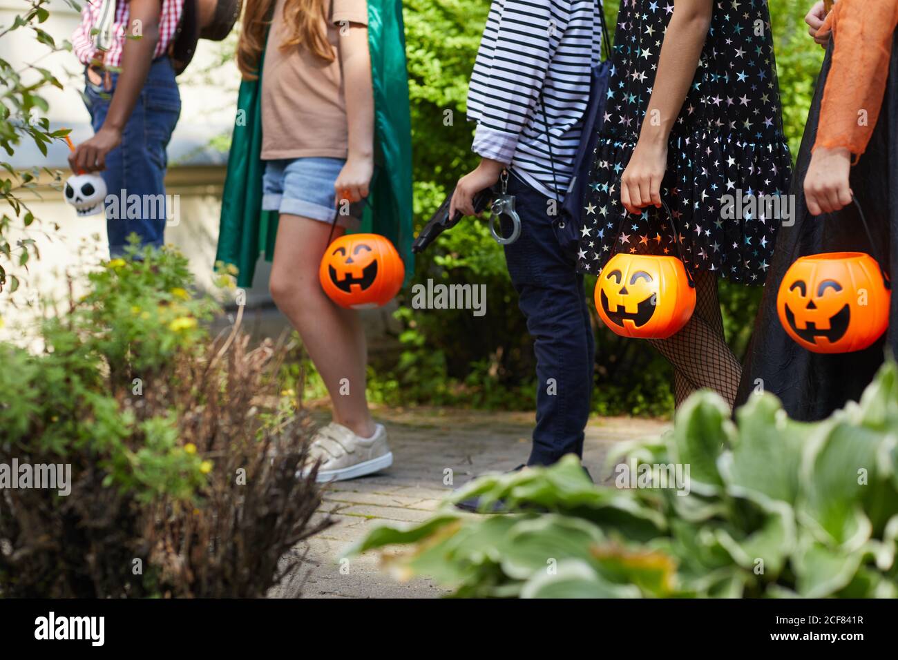 Gros plan d'enfants debout dans une rangée et tenant des sacs sous forme de citrouilles, ils attendent des gâteries à l'extérieur Banque D'Images