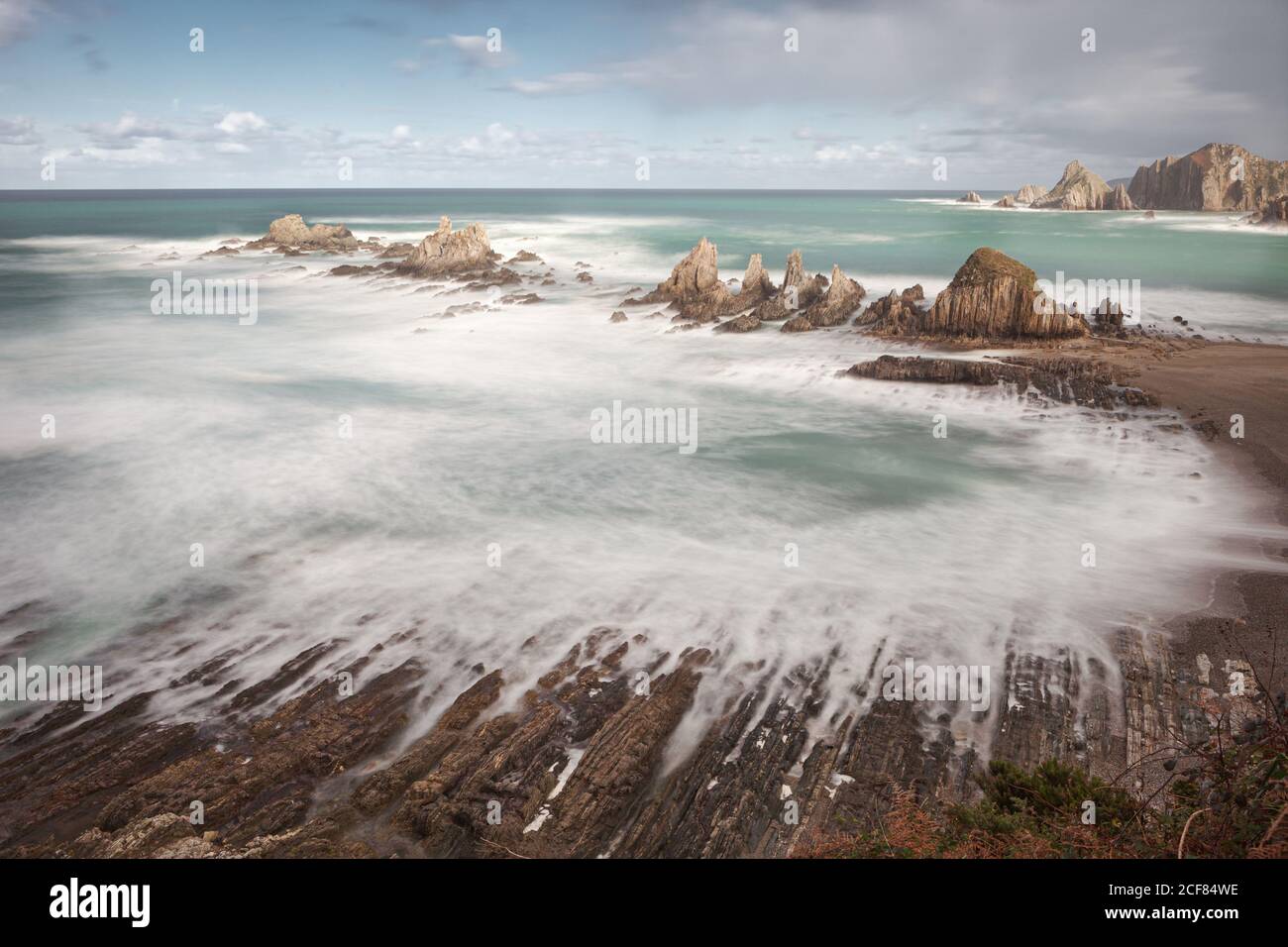 De dessus l'eau turquoise claire et les vagues de mousse blanche troublée Sur la plage de la Gueirua avec une incroyable érosion dans la composition avec formations rocheuses nettes sous un ciel bleu couvert de nuages moelleux En Espagne Banque D'Images