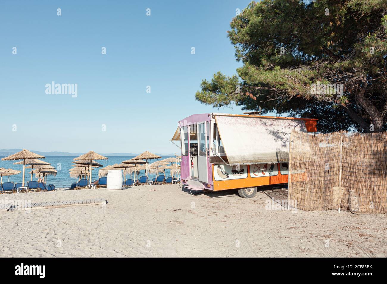 Plage de sable avec parasols en chaume et camion de nourriture en plein soleil, Grèce Banque D'Images