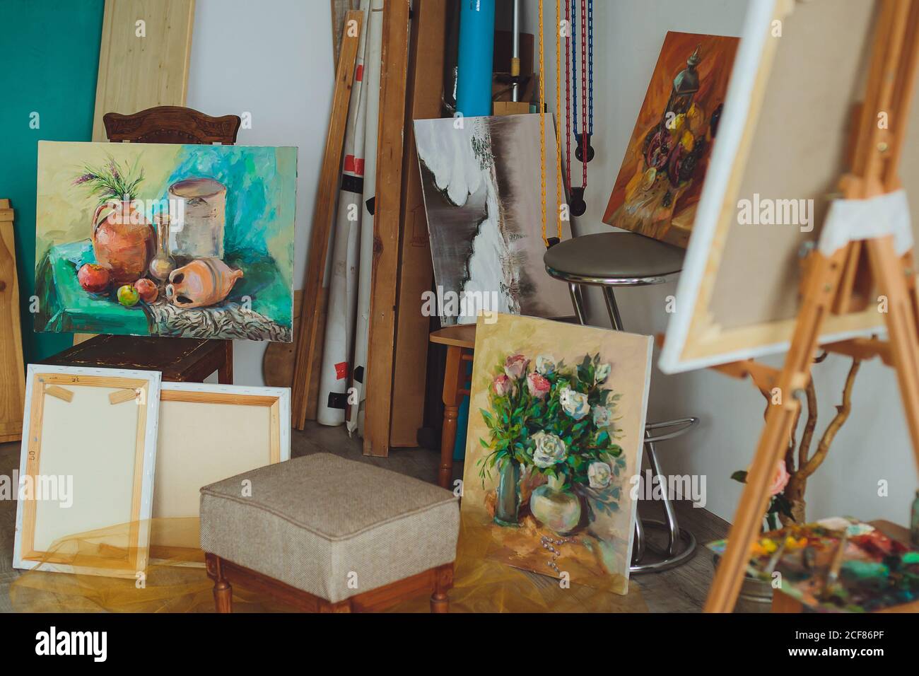 Intérieur d'un studio de peintres ou d'une galerie avec des toiles colorées couvrant une variété de sujets suspendus sur le mur et un tableau inachevé sur un woo Banque D'Images