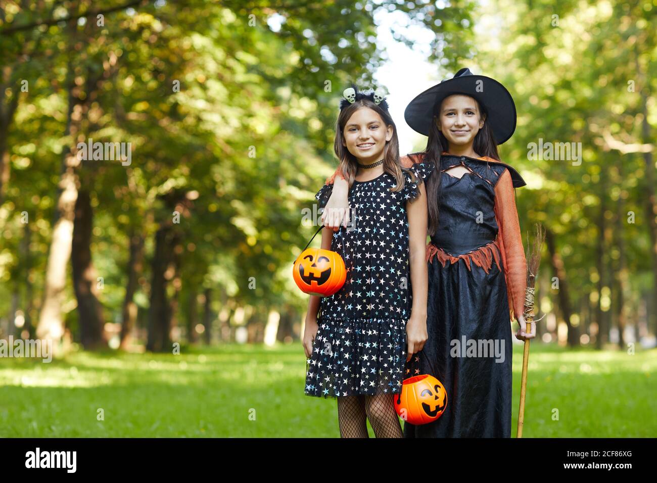 Portrait de deux filles en sorcières costumes souriant à l'appareil photo en vous tenant dans le parc à l'extérieur Banque D'Images