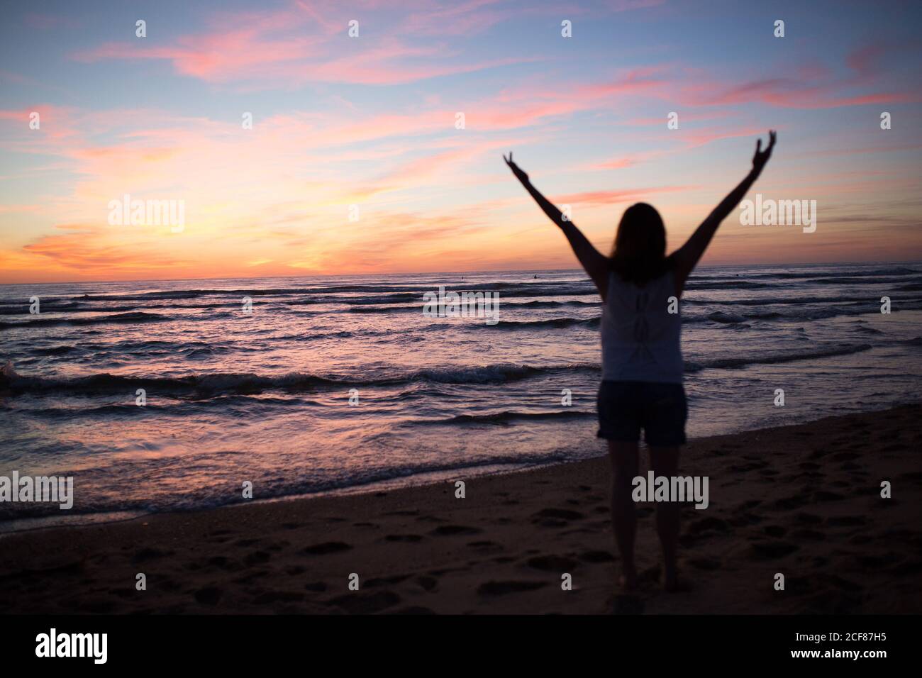 Femme avec les mains levées pendant la marche sur la plage de sable contre ciel pittoresque au coucher du soleil Banque D'Images