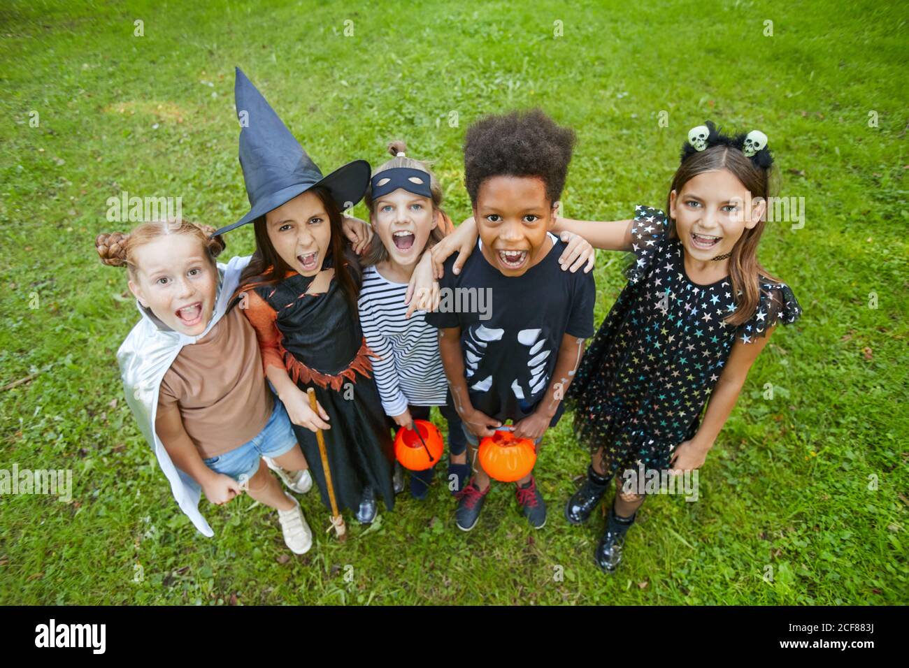 Groupe d'enfants en costumes d'Halloween criant à la caméra pendant sur l'herbe verte à l'extérieur Banque D'Images