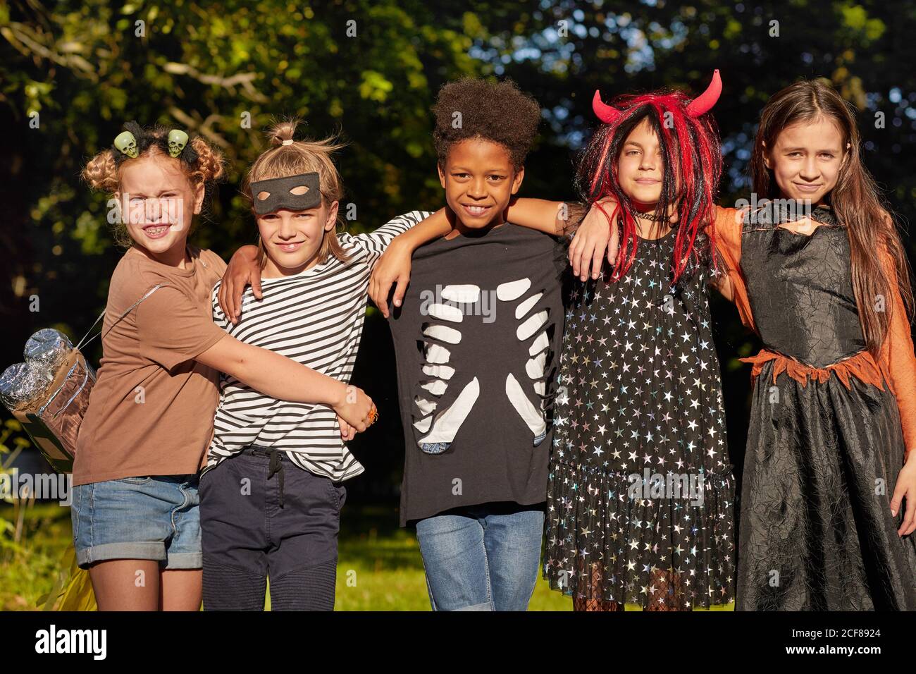 Portrait des filles et des garçons en costumes d'Halloween embrassant chacun autre et regarder la caméra en se tenant dans le parc Banque D'Images